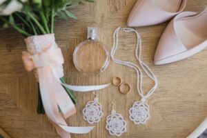 Bridal accessories laid out neatly with shoes, rings, perfume, earrings, necklace, and bouquet