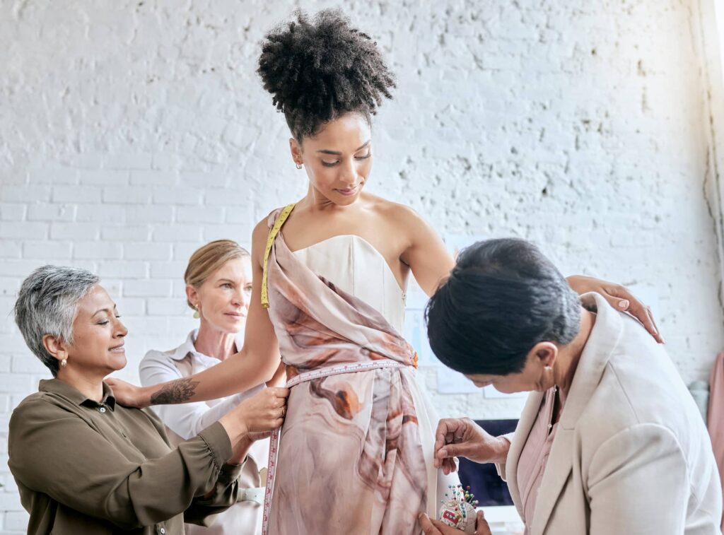 Seamstresses fitting and pinning a dress on a client during a tailoring appointment