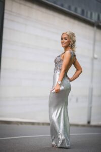Woman wearing a full-length silver prom gown with embellished bodice and sleek silhouette
